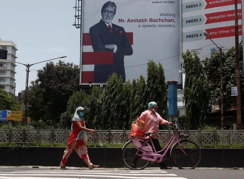 People wearing protective masks walk in front of a hoarding of Bollywood actor Amitabh Bachchan wishing him a speedy recovery, as he and members of his family were tested positive for coronavirus disease (COVID-19) in Mumbai, India, July 19, 2020. REUTERS/Francis Mascarenhas